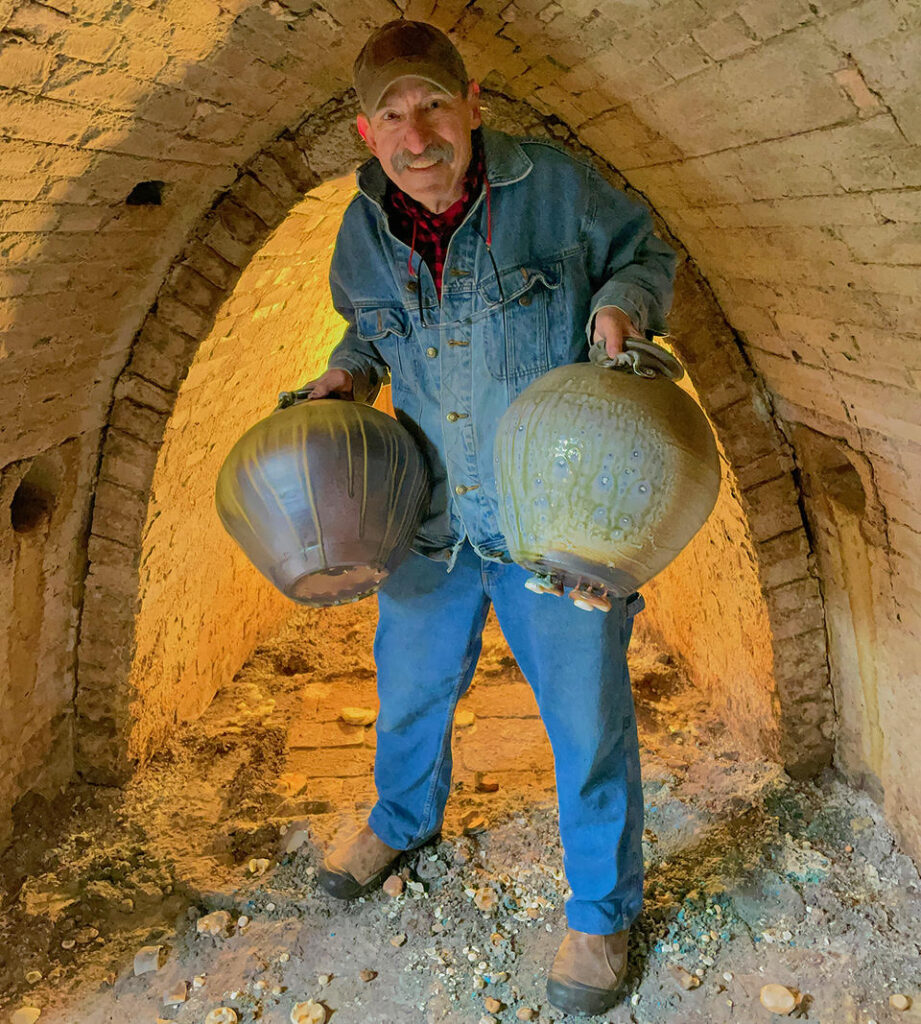 Potter holding two wood-fired jars inside a brick kiln